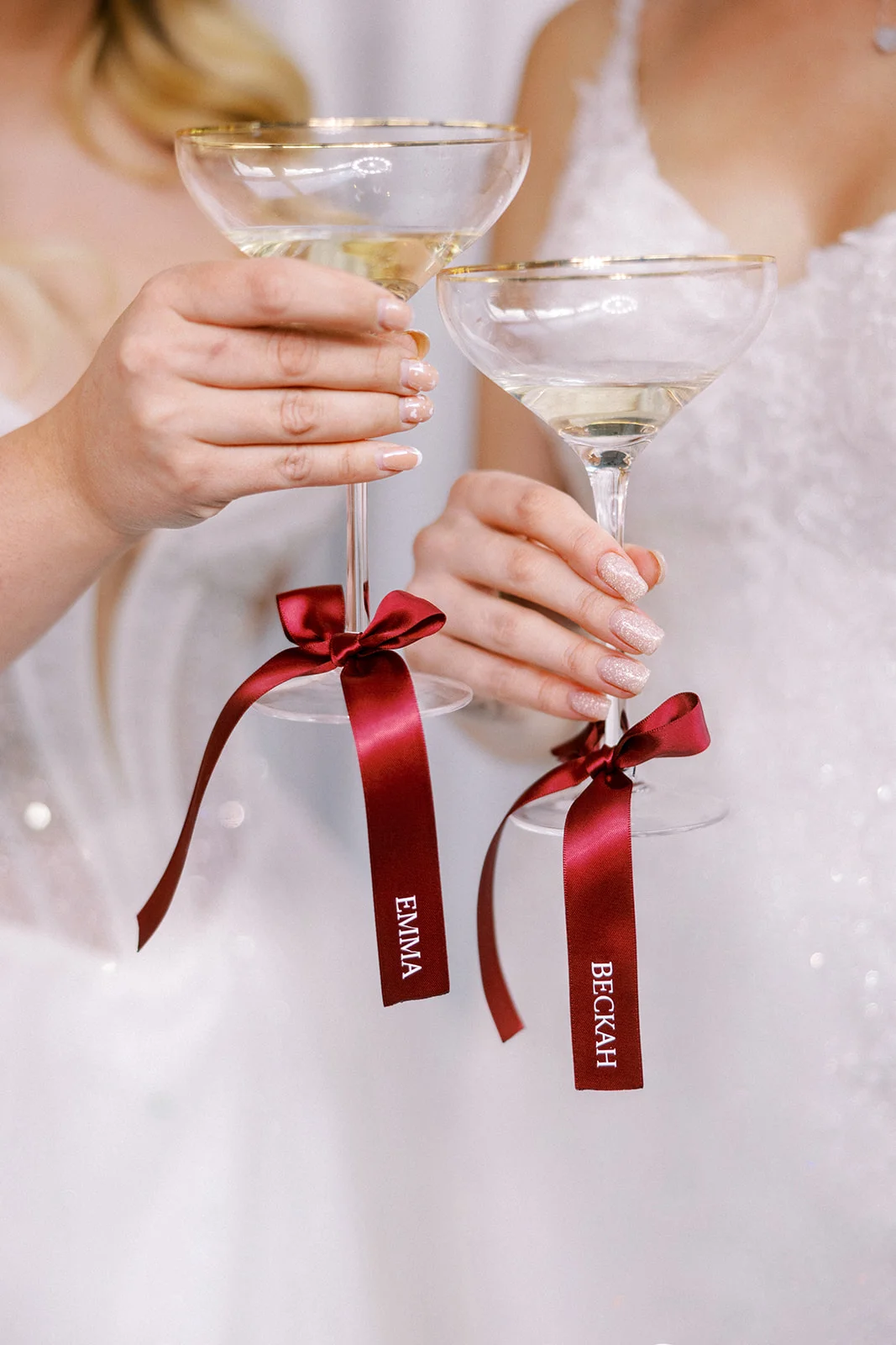 Cranberry red ribbons tied to wedding coupe toasting glasses with the brides names on each