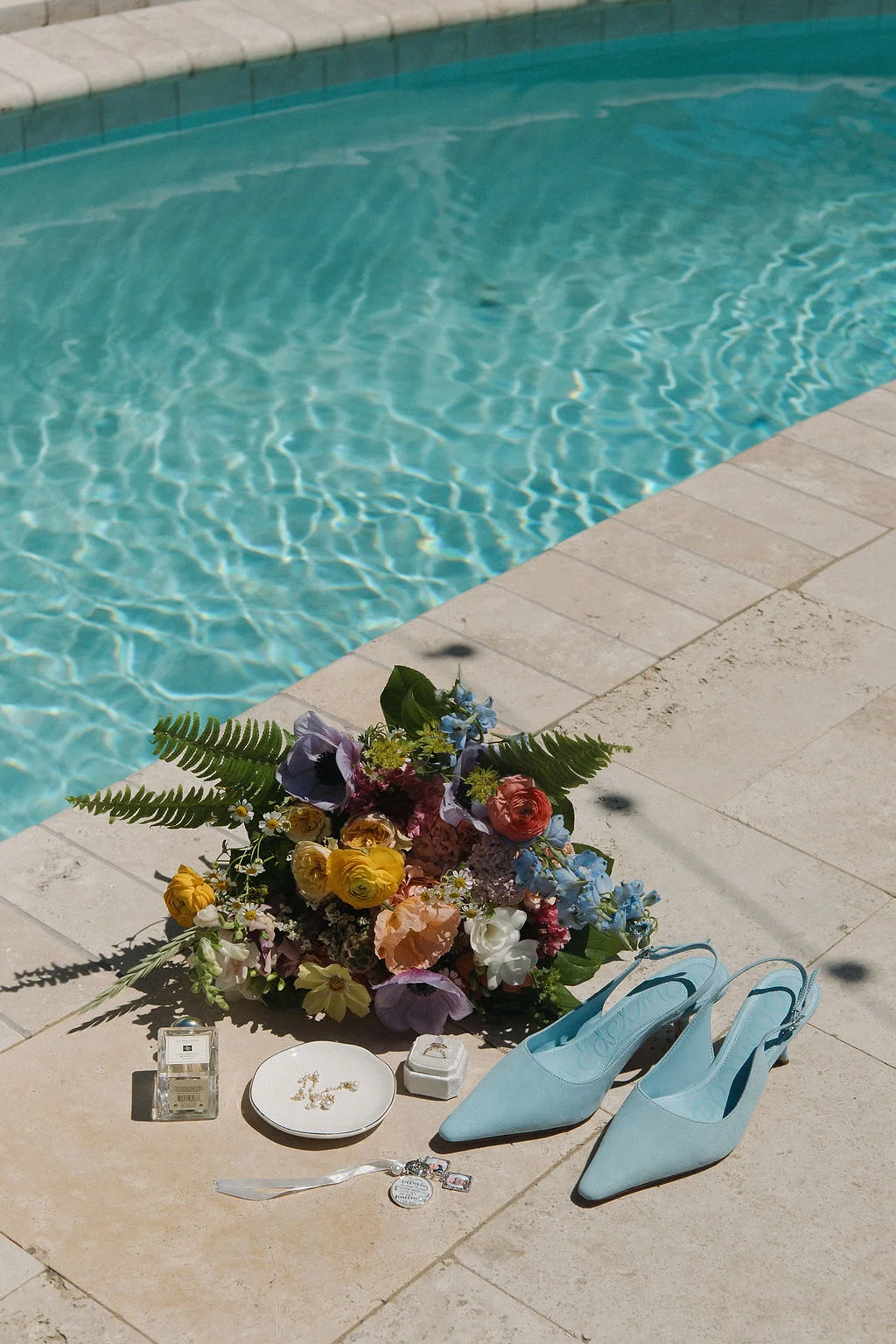 Bridal details that include blue pointed toe heels, wedding jewelry, and perfume by the beach house pool
