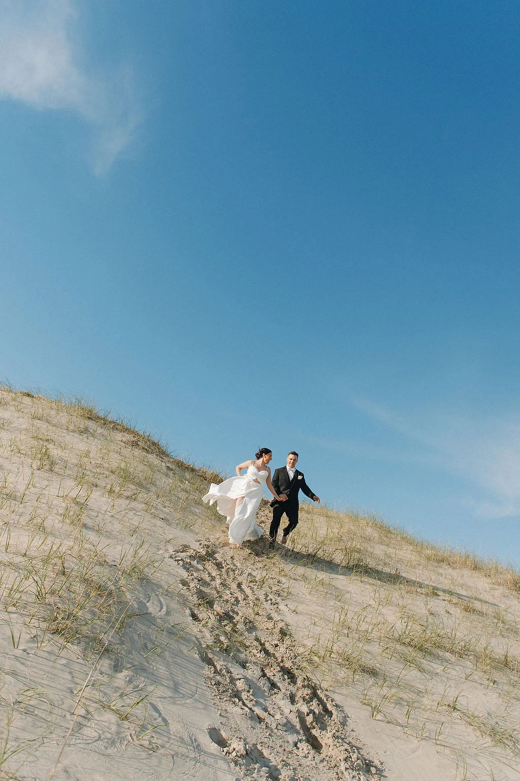 Bride and groom running down sand dunes in Corolla