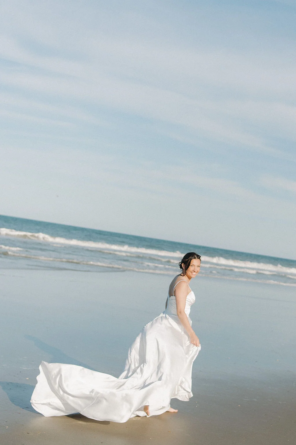 Carefree bride running on the Corolla beach in her wedding dress