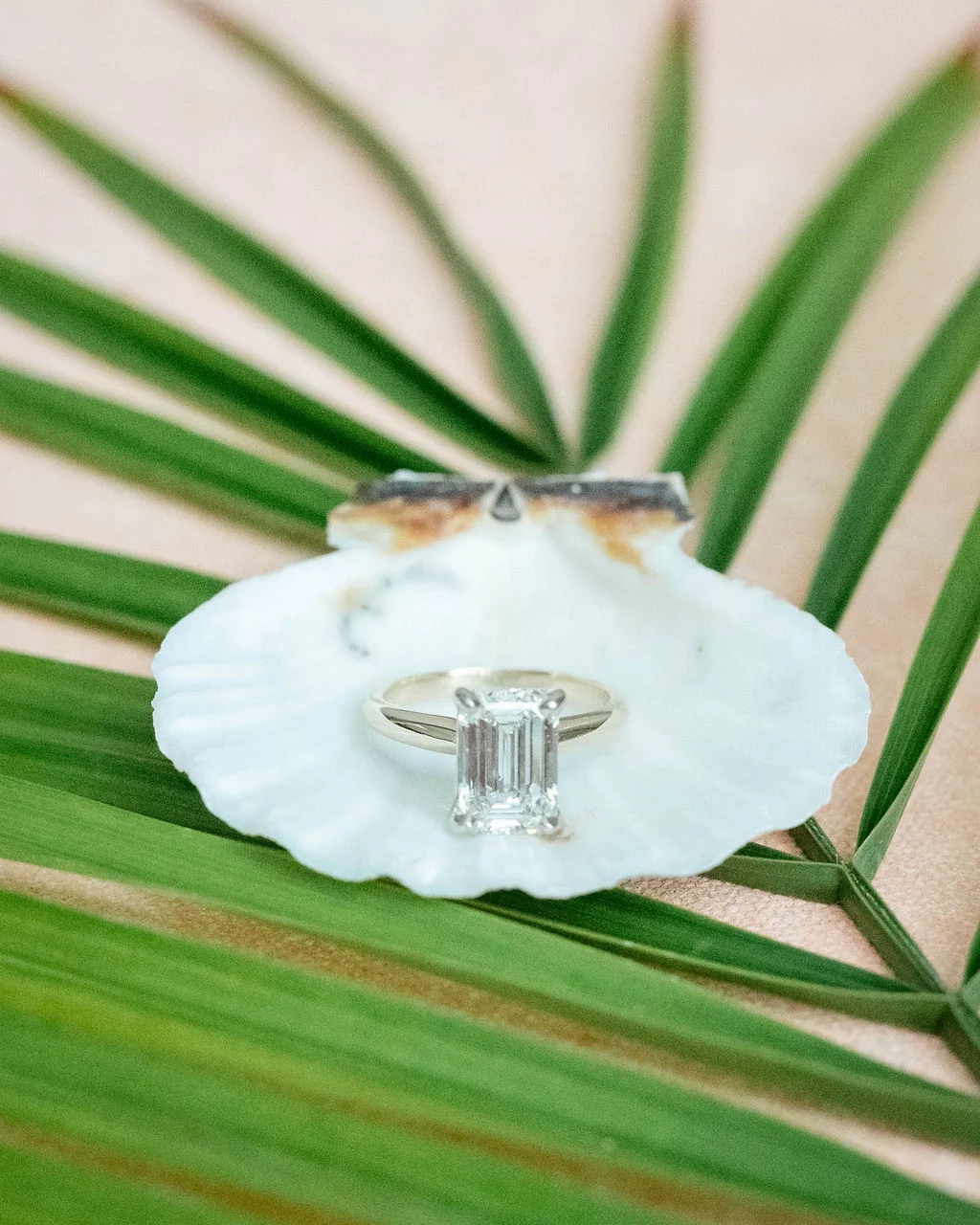 Emerald cut diamond engagement ring sitting on a seashell and palm leaves for beach wedding