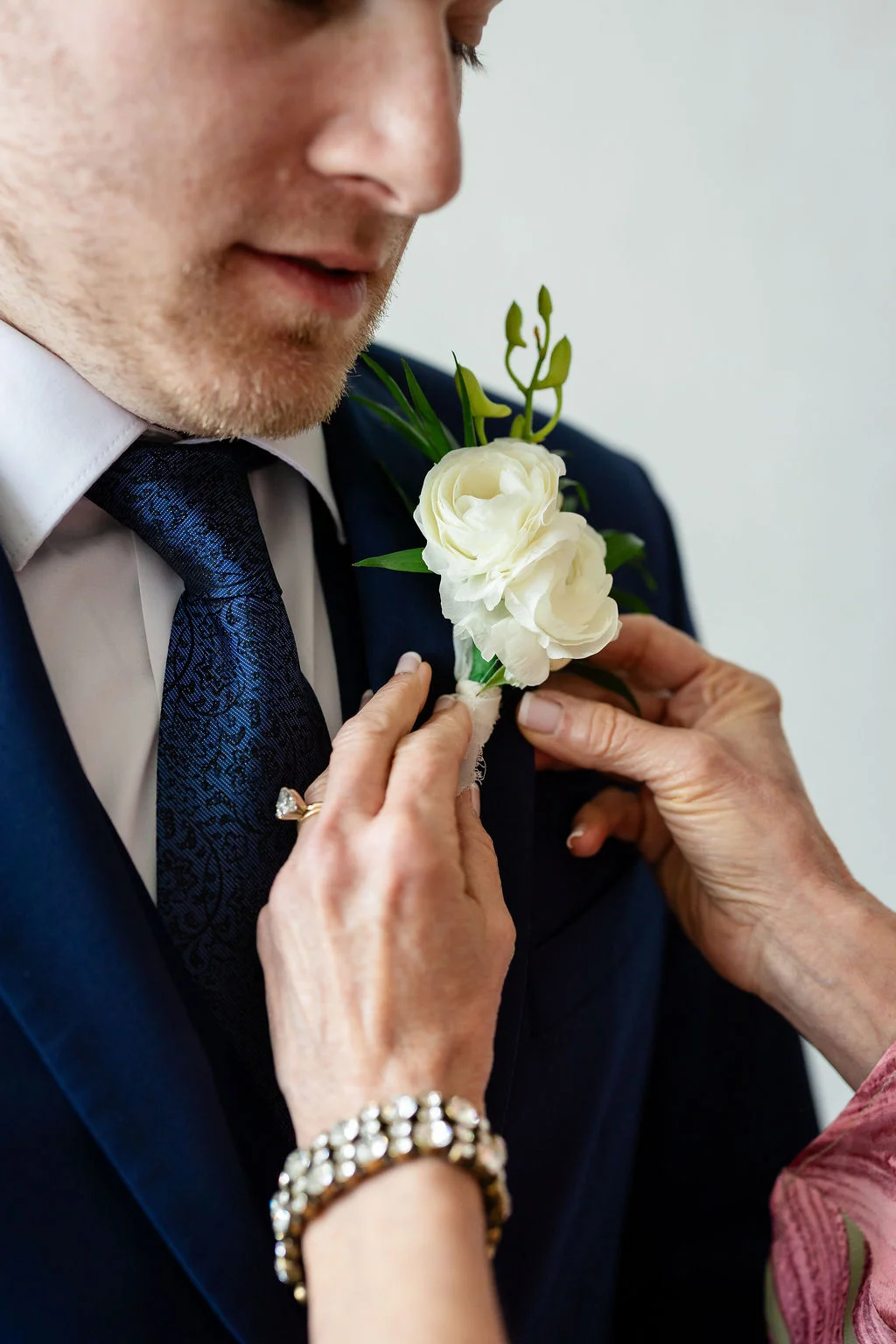 Groom putting on his all white boutonniere with ranunculus and orchids