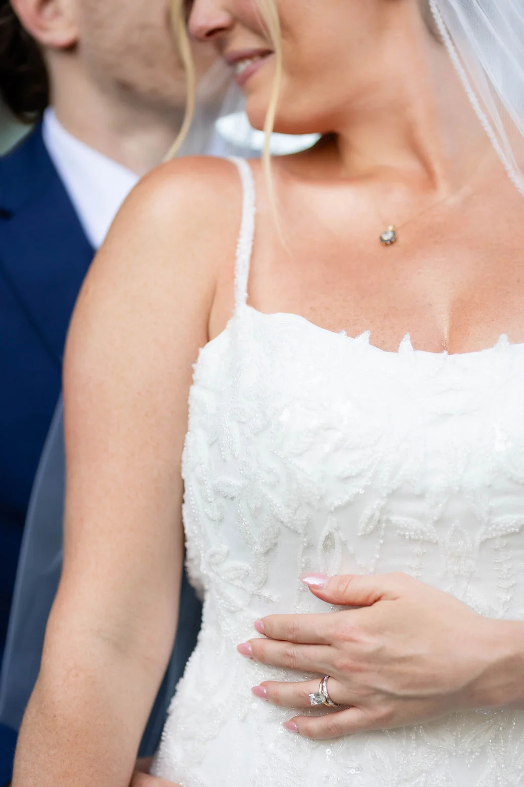 Closeup of a bride's beaded wedding dress and emerald cut wedding rings