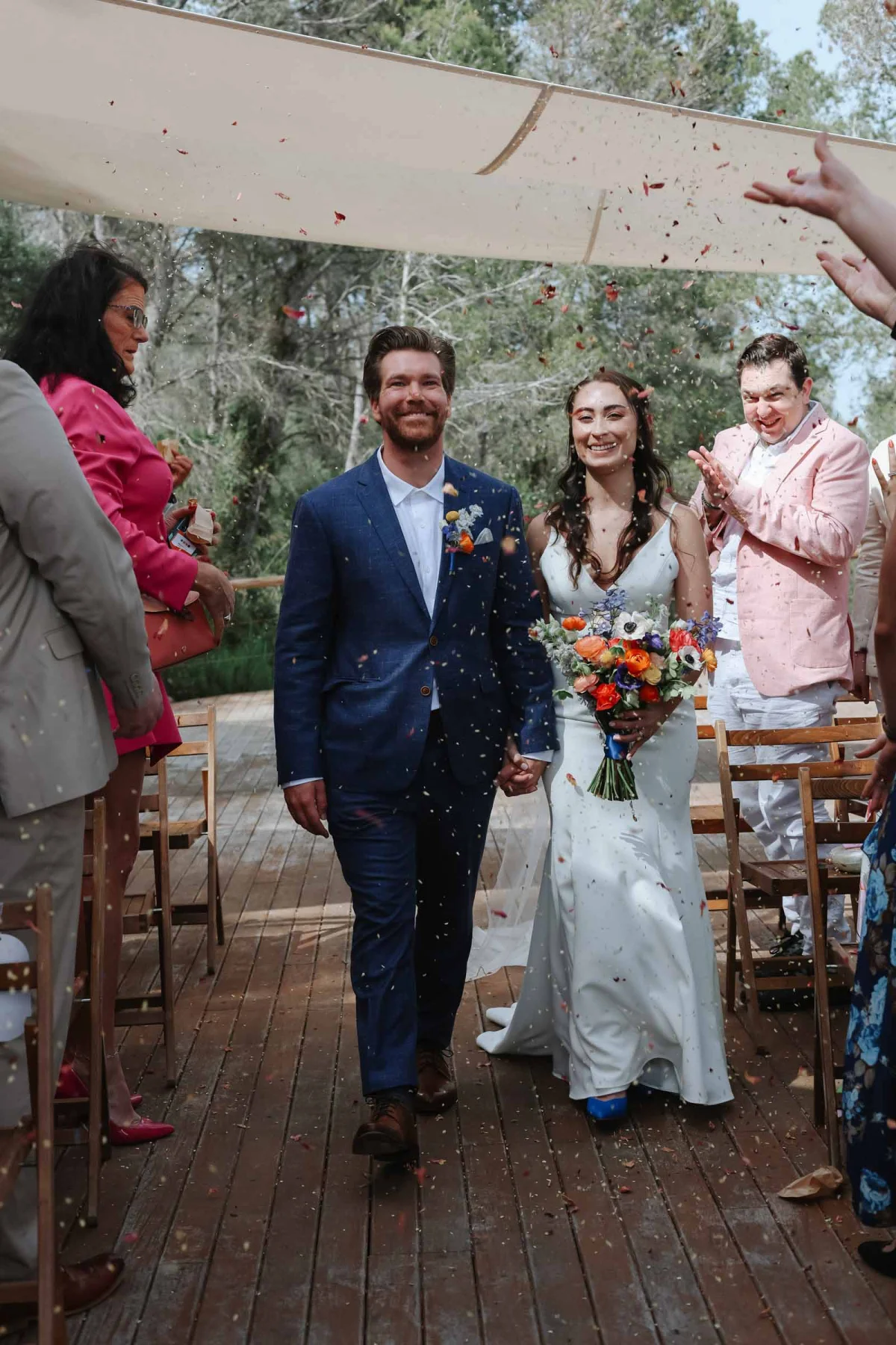 Bride and groom walking down the aisle with guests tossing flower petal confetti to celebrate