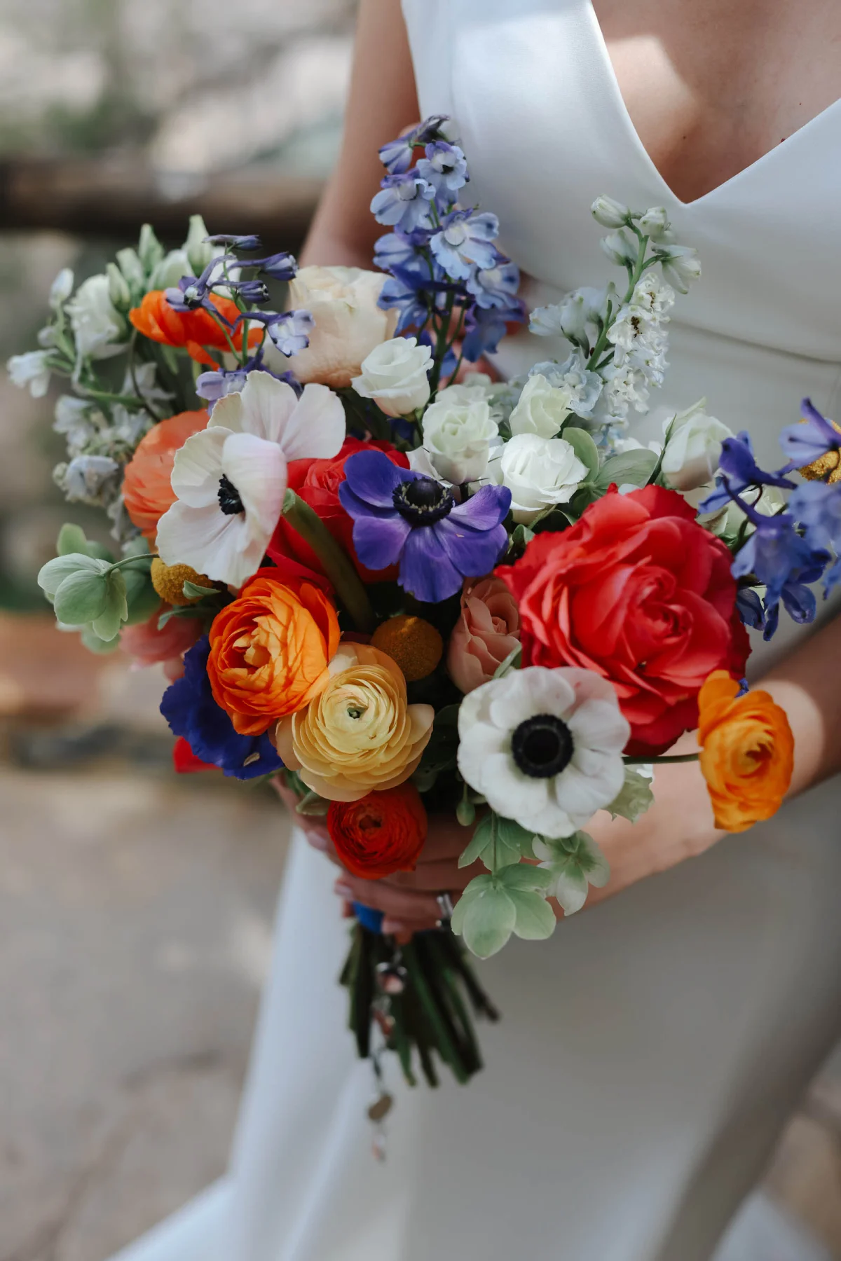A colorful wedding bouquet with purple and white anemones and orange, red, and yellow ranunculus.