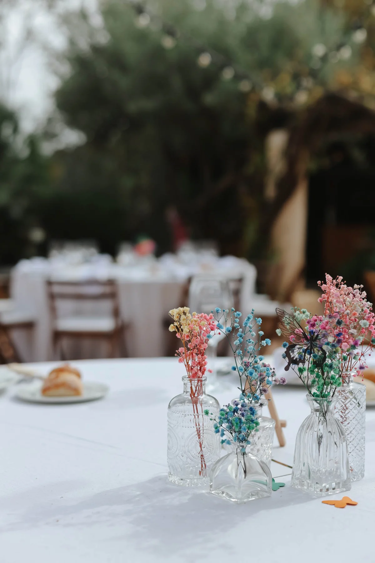 Colorful rainbow dyed Gypsophila or babys breath in mismatched vintage bud vases with butterfly cutouts for simple wedding centerpiece