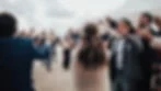 Woman with floral headband celebrates with crowd holding sparklers and drinks, outdoors under a cloudy sky. Festive and joyful mood.
