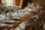 Elegant tablescape with arranged plates, crystal glasses, and woven placemats. Blue and white floral centerpieces adorn the wooden table.