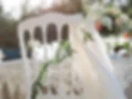 White chair with lace table setting, adorned with white fabric and greenery. Soft natural light creates a romantic, elegant ambiance.