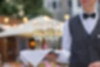 Waiter holding a tray of champagne glasses at an outdoor event. Warm lights and green foliage in the blurred background create an elegant atmosphere.