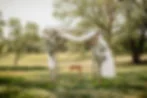 Outdoor spring wedding ceremony arch adorned with white flowers and flowing draping, set in a lush green park