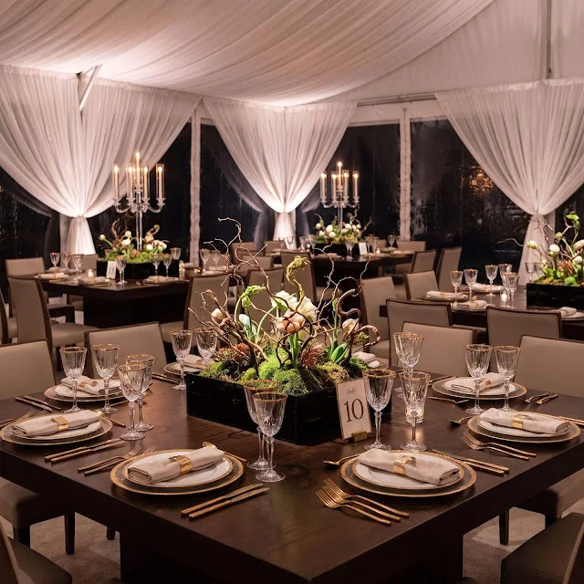 High-end indoor tented wedding reception with dark wood tables and elegant centerpieces.