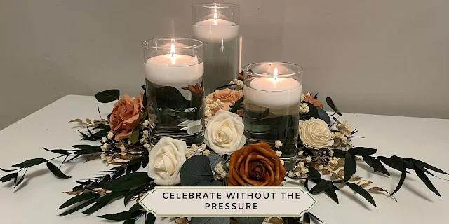 Three glass cylinder vases with white floating candles, terracotta and ivory roses, baby’s breath, and eucalyptus on a white reception table.