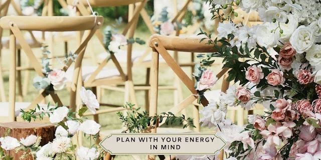 Outdoor wedding ceremony with light wood cross-back chairs on a lawn, framed by a lush installation of white and pink roses.