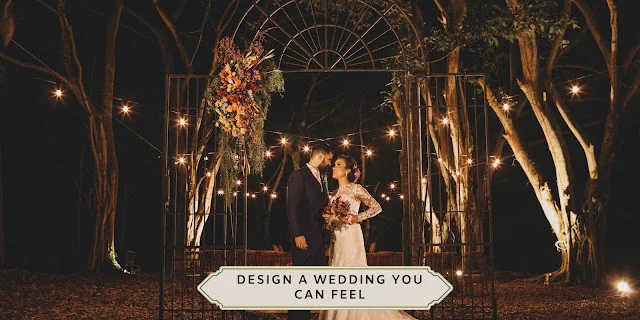 WEDDING ATMOSPHERE AND SENSORY DESIGN Couple standing beneath a dramatic floral installation and warm string lights at an outdoor evening wedding reception.