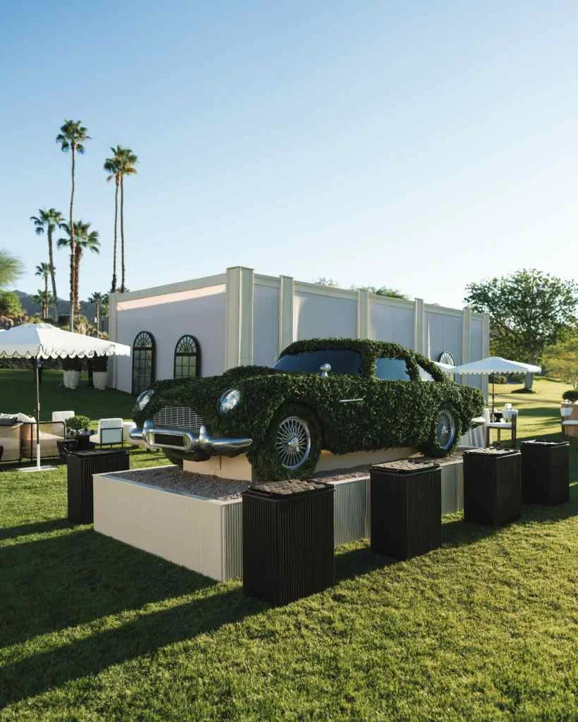 Vintage black car displayed outdoors at a wedding venue with palm trees and white tents.