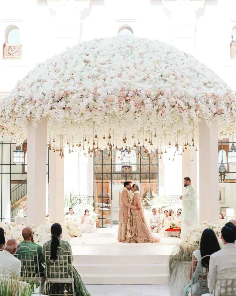 Elegant wedding ceremony under a floral canopy with guests and officiant present.