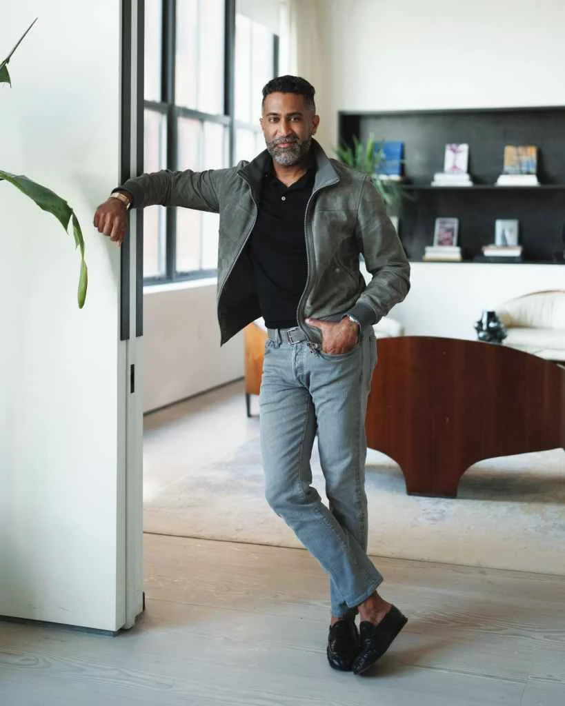 Stylish man in casual attire standing in modern living room with large windows.